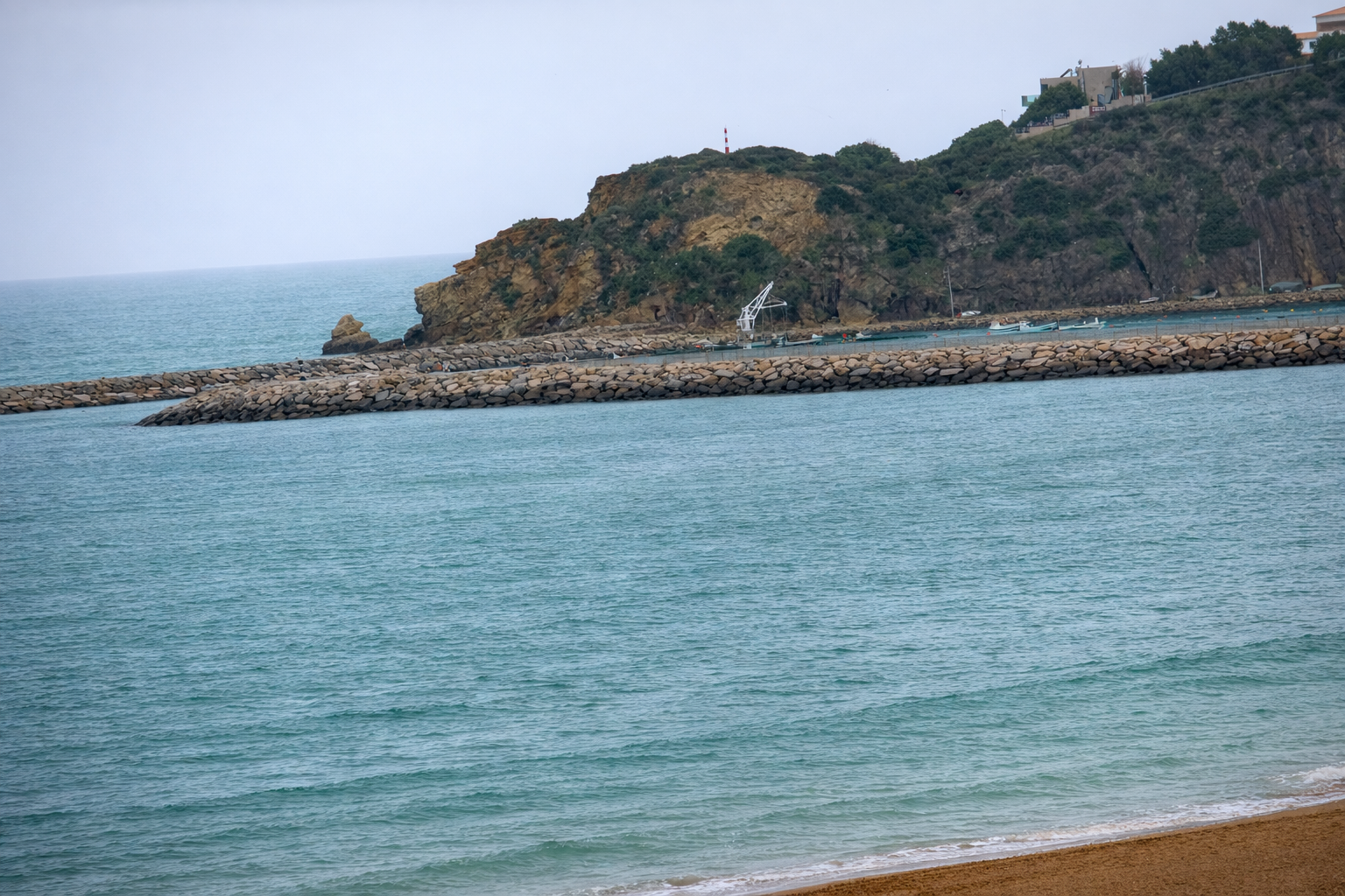 Costa rochosa com farol e quebra-mar